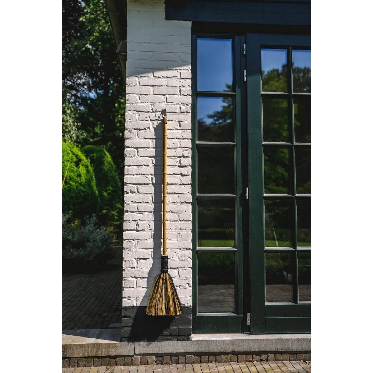 Bohemian-style Indonesian grass broom against a white brick wall, perfect for interior decor, by Bazar Bizar Living.
