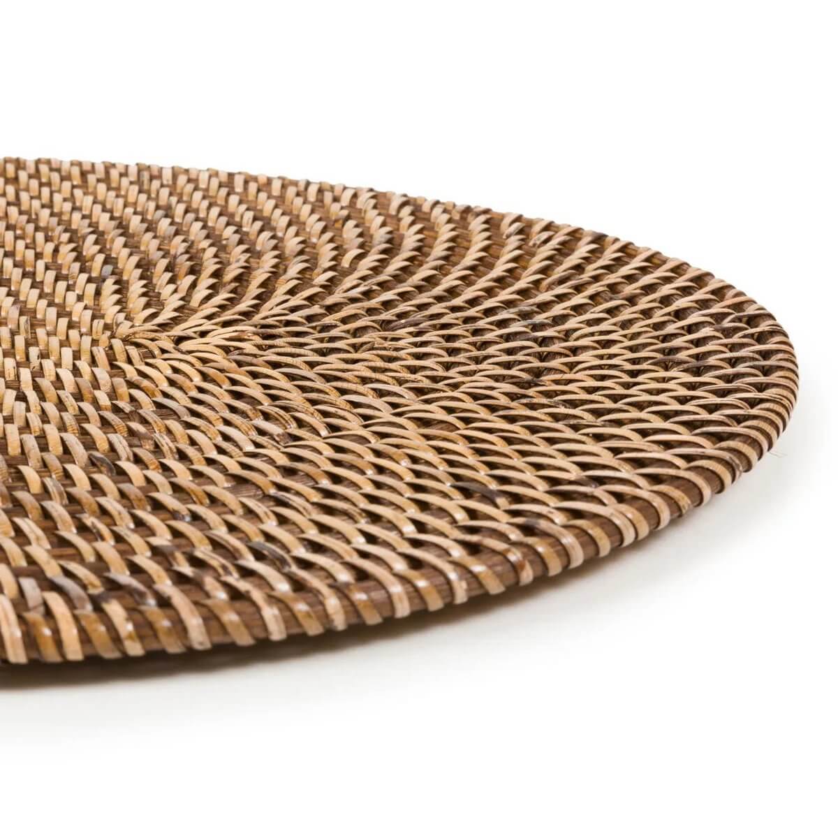 Close-up of a handwoven natural brown oval rattan placemat, perfect for a Bohemian island-style table setting by Bazar Bizar Living.