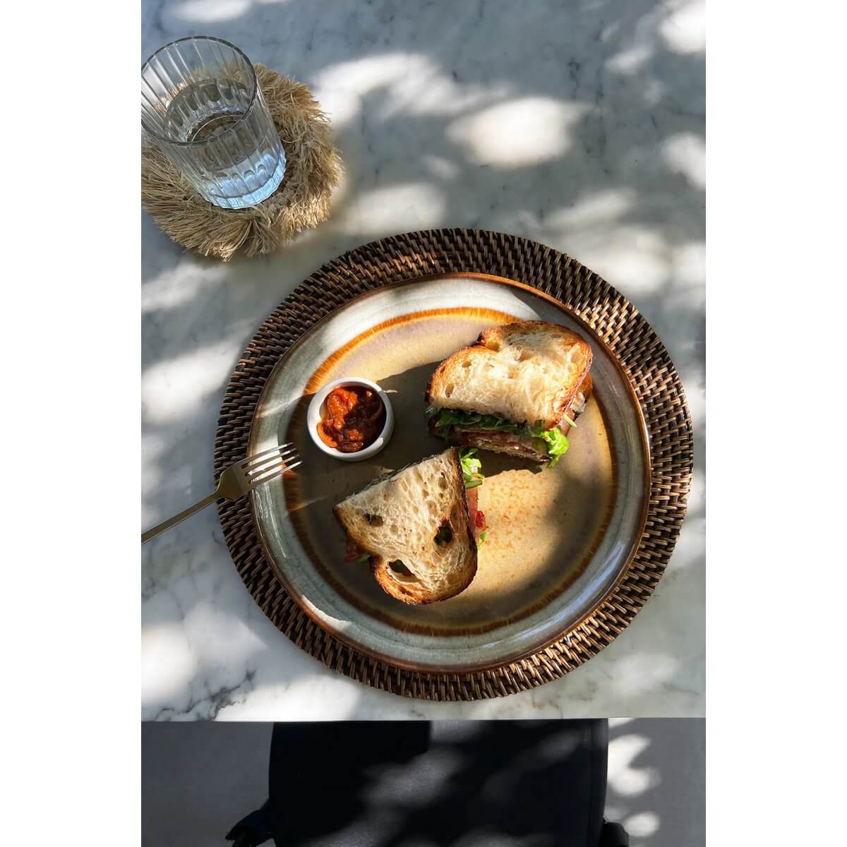 "Bohemian colonial placemat with a rustic sandwich and dip, styled on a marble table, showcasing natural island aesthetic."