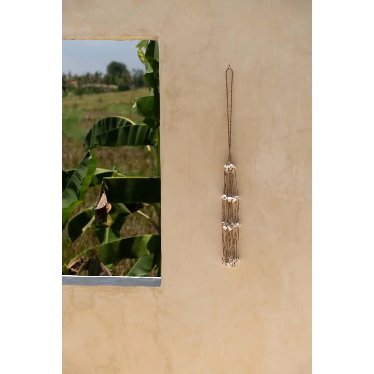 Bohemian white shell hanger on beige wall, handmade by Balinese artisans, adding exotic charm to doors, curtains, or walls. 8x75cm by Bazar Bizar.