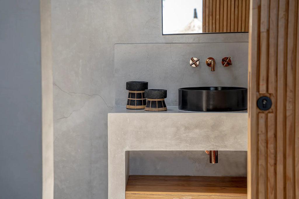 Moderne badkamer met De Serene kaarsenhouders in zwart terracotta en rotan op betonnen wastafel.
