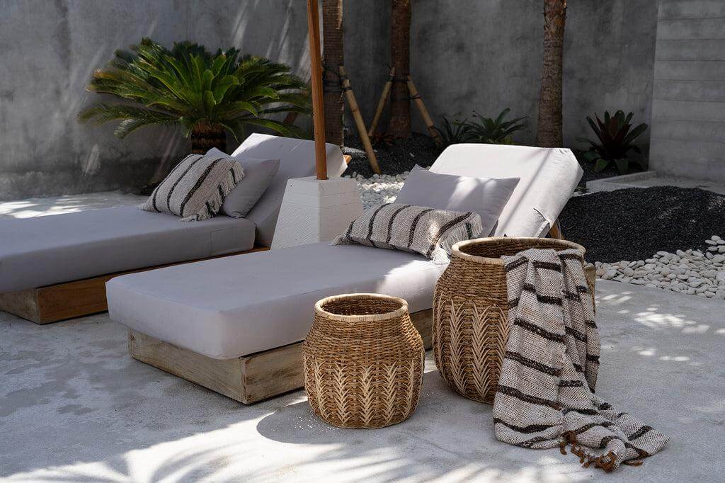 Stijlvolle bohemian tuinsetting met handgeweven plaid, kussens op ligbedden en rieten manden. Perfect voor gezellige buitenavonden.