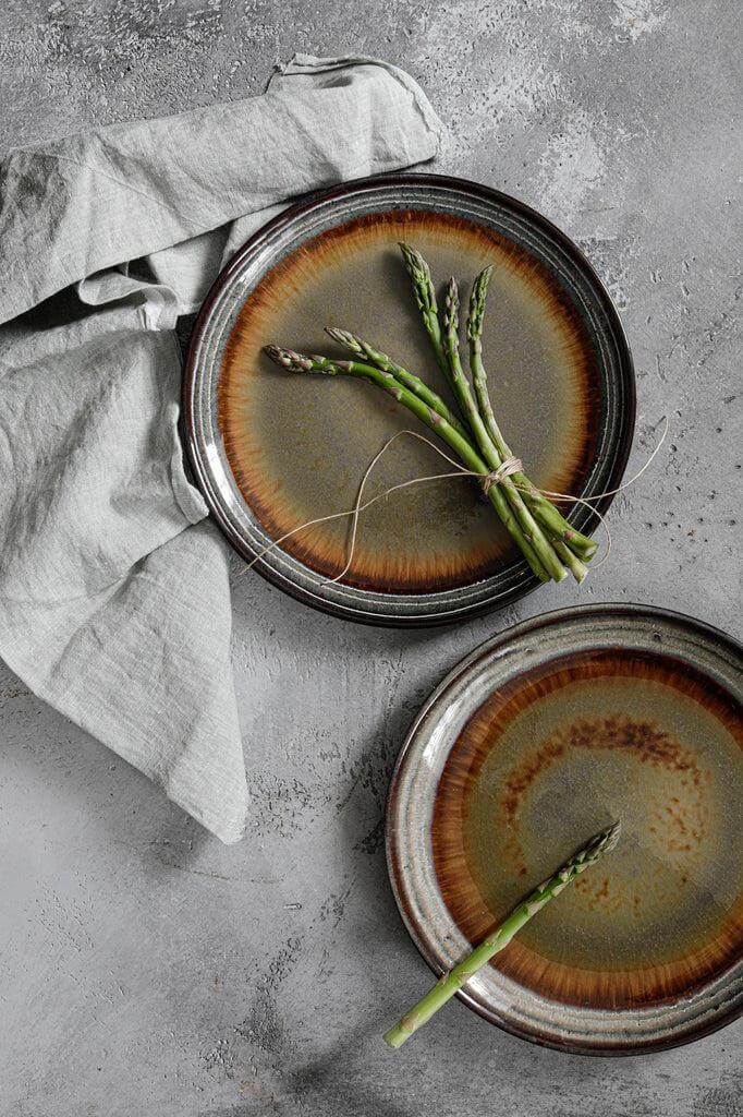 Elegante Portugese keramische borden met groene asperges op een rustiek gedekte tafel, uit de Comporta Collectie met craquelé afwerking.