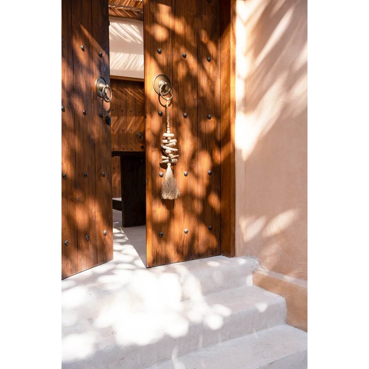 Bohemian raffia tassel hanging on a rustic wooden door, creating an exotic vibe. Ideal for home decor by Bazar Bizar Living.