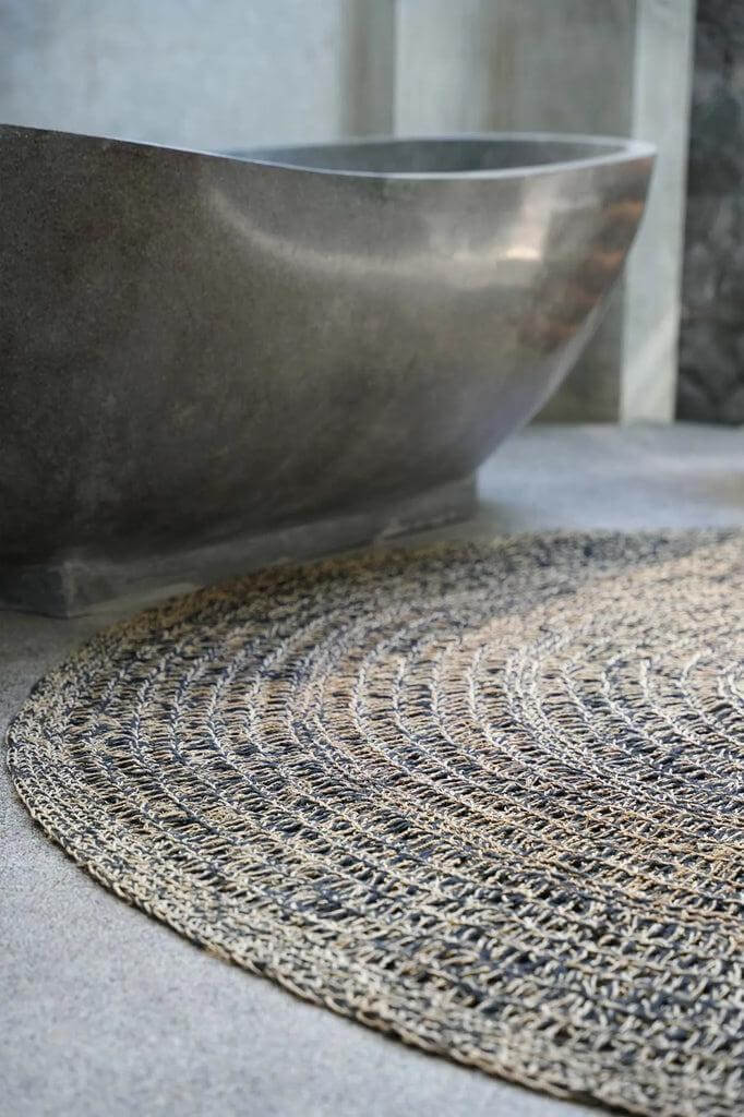 Cirkelvormig zeegras tapijt in natuurlijke en zwarte tinten voor textuur en zachtheid op een harde vloer naast een minimalistisch bad.