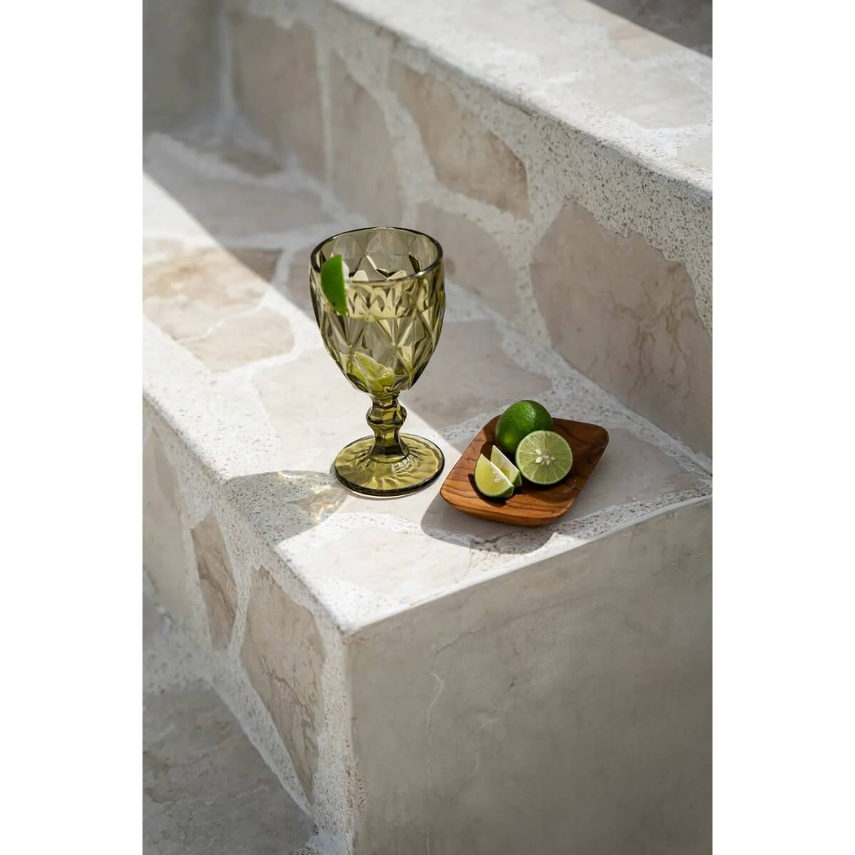 Bohemian style rustic setting with a green glass goblet and teak root rectangular dish holding limes on a stone step.