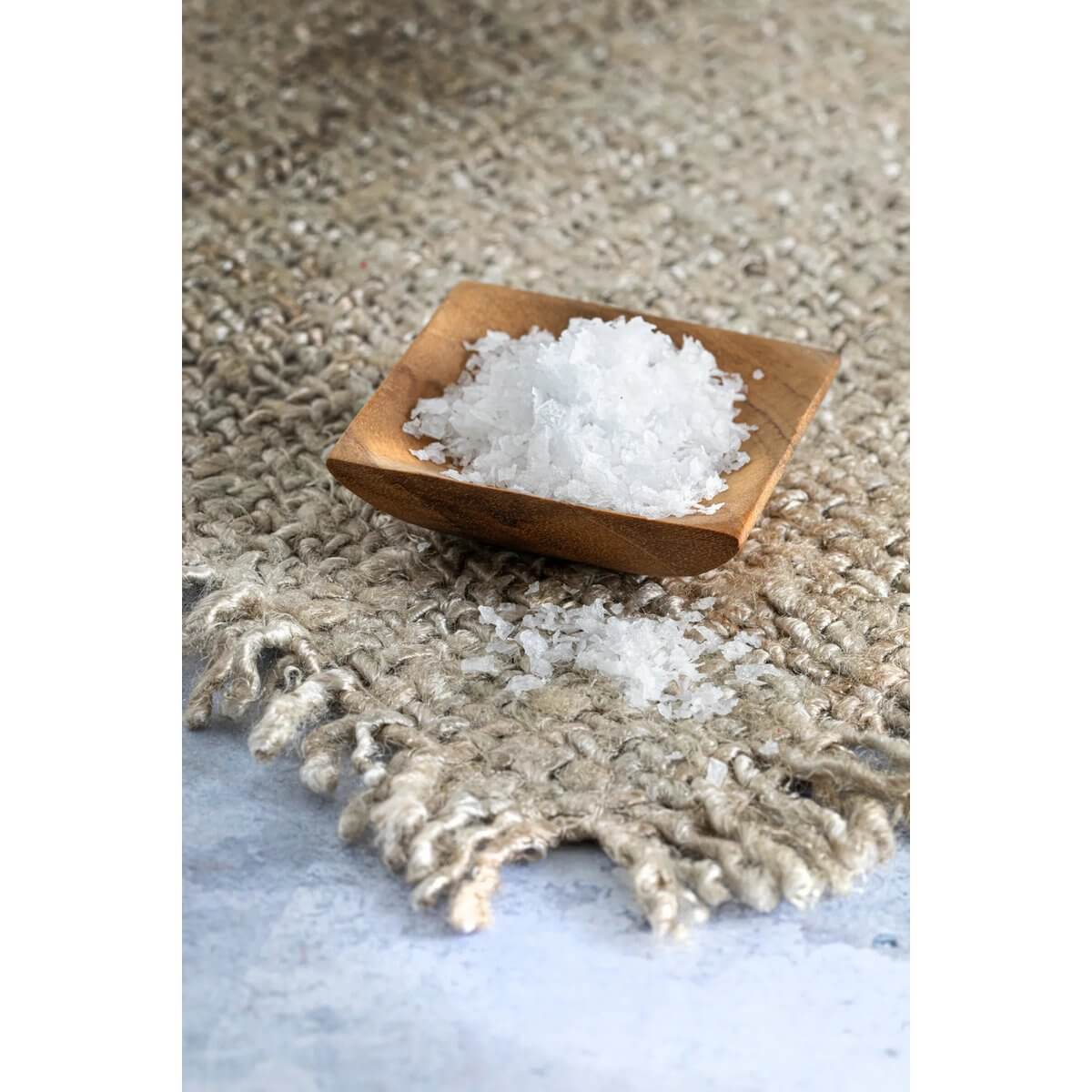 Het Teakwortelzoutbakje - XS with coarse salt, showcasing a bohemian-style teakhouten bowl on a textured fabric.