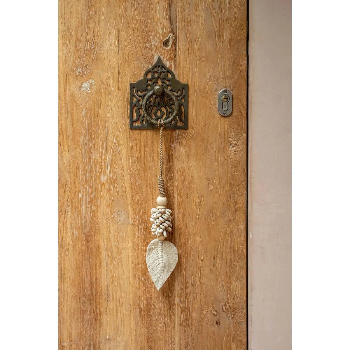 Bohemian shell tassel hanging on a rustic door for exotic home decor, handmade by Balinese artisans. Bazar Bizar Living.