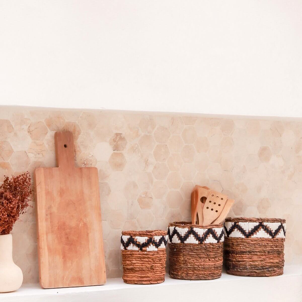 Kleine opbergmand SADARA met macramé patroon naast houten snijplank en keukenaccessoires op een aanrecht.