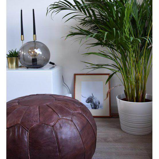 Chocoladebruine Marokkaanse leren poef in een moderne woonkamer met planten en decoratieve accessoires.