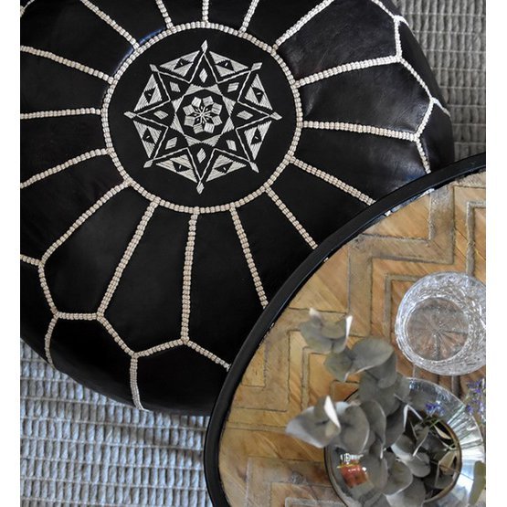 Zwarte leren poef met Marokkaans patroon naast een glazen tafel, perfect voor een gezellige boho sfeer in je interieur.