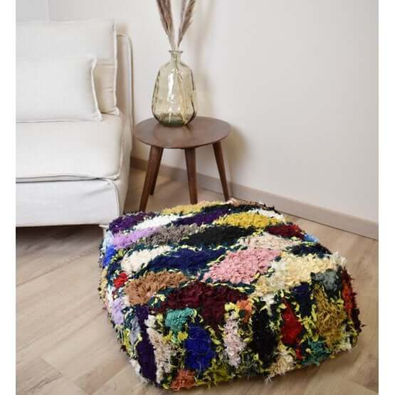 Kleurrijk Marokkaans Boucharouite vloerkussen naast een moderne bank, handgemaakt van gerecycled textiel.