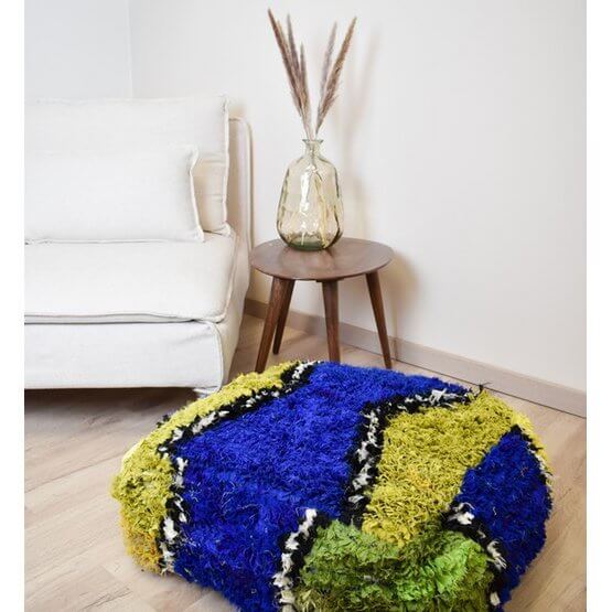 Marokkaans Boucharouite vloerkussen K1474 in levendige kleuren, handgemaakt van gerecycled textiel, naast moderne stoel en tafeldecor.