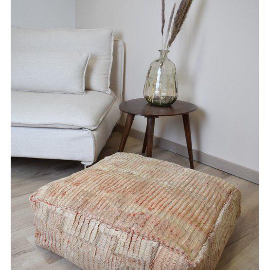 Marokkaans vloerkussen voor bohemian interieur, handgemaakt van vintage Berberkleed, gelegen naast een moderne bank en houten bijzettafel.