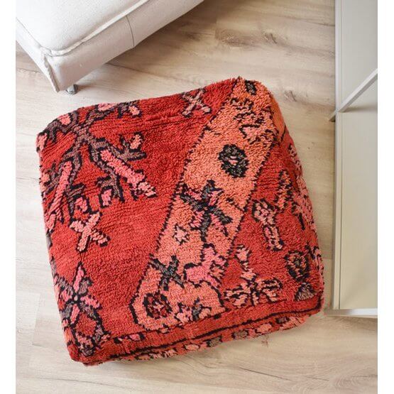 Vintage Marokkaans vloerkussen met Berberpatroon, warme rode tinten, bohemian sfeer, uniek handgemaakt item op houten vloer.