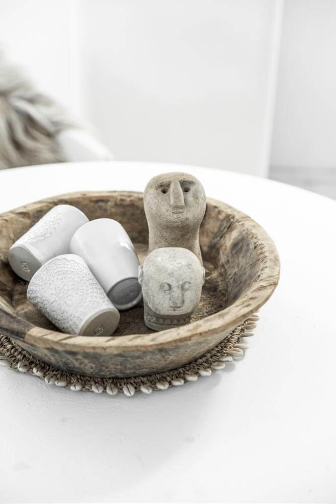 Houten schaal met decoratieve stenen en kaarsen op een placemat met schelpaccenten, perfect voor een boho interieur.