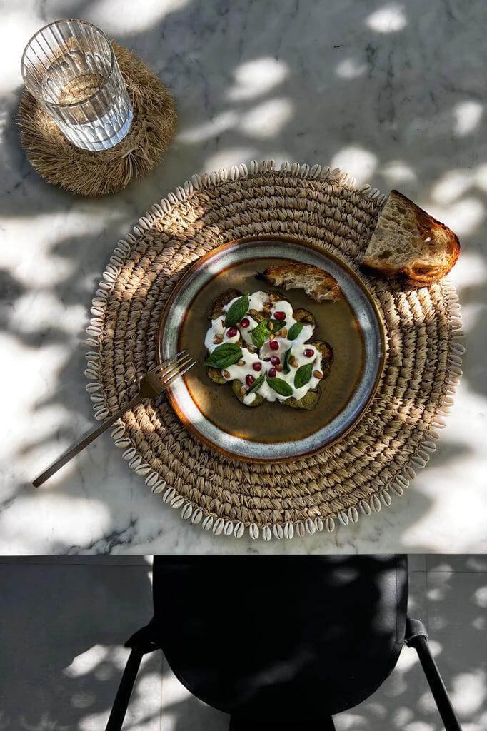 Raffia placemat met kauri schelpen, boho tafelsetting met brood en gerecht, past perfect bij Ibiza & Bali spiegels.