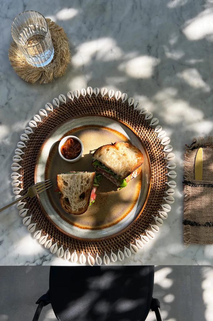 Lunch op rotan placemat met schelpen, brengt eilandstijl naar je tafel. Tropisch interieur met boho vibes. Perfect voor Ibiza & Bali look.