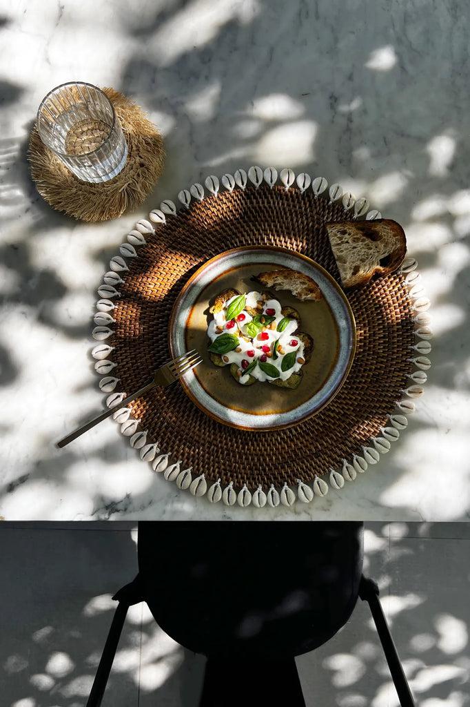 Handgeweven rotan placemat met kauri schelpen, perfect voor een tropische eilandstijl tafelsetting.