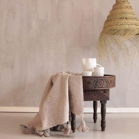 Alt Tag: Gezellige camel-kleurige pompom deken op houten tafeltje, perfecte aanvulling voor een boho interieur.
