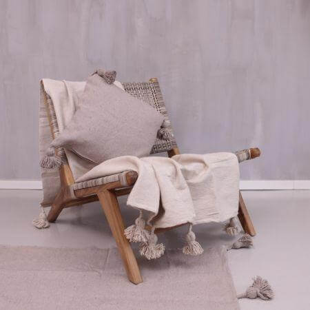 Gezellige beige Pompom deken over een houten stoel in een modern interieur, perfect voor een ontspannen avond met muntthee.