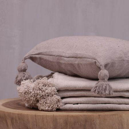 Alt Tag: Stapel pompom dekens in beige op houten tafel voor knus interieur.