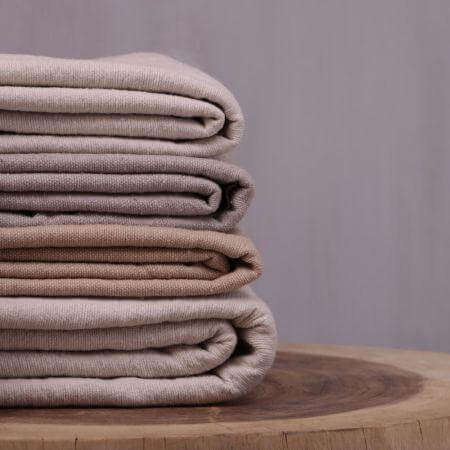 Gestapelde beige Pompom dekens op een houten ondergrond, perfect voor een cozy boho avond op de bank met een kopje muntthee.