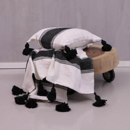 Zwart-wit gestreepte pompom deken en kussen op een houten roltafeltje, perfect voor een gezellige avond op de bank.