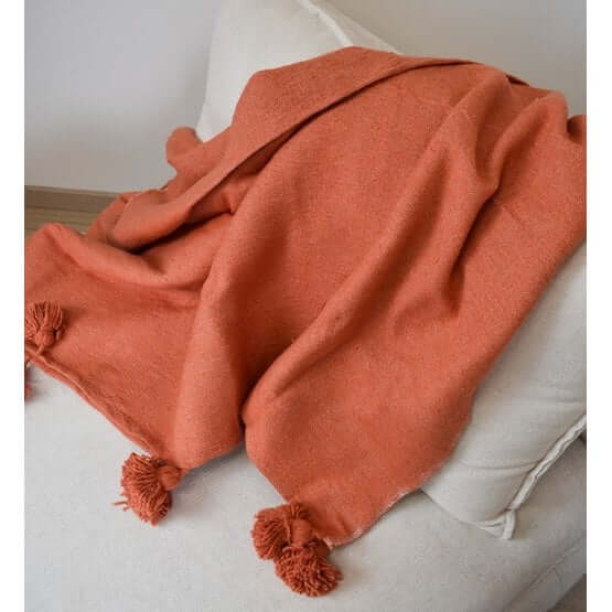 Oranje Marokkaanse pompondeken op bank, ideaal als knusse woonaccesoire voor moderne en bohemien stijlen.