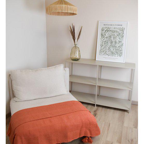 Gezellige kamer met beige stoel bedekt met oranje Marokkaanse pompondeken, naast minimalistisch rek en stijlvolle plant op vaas.