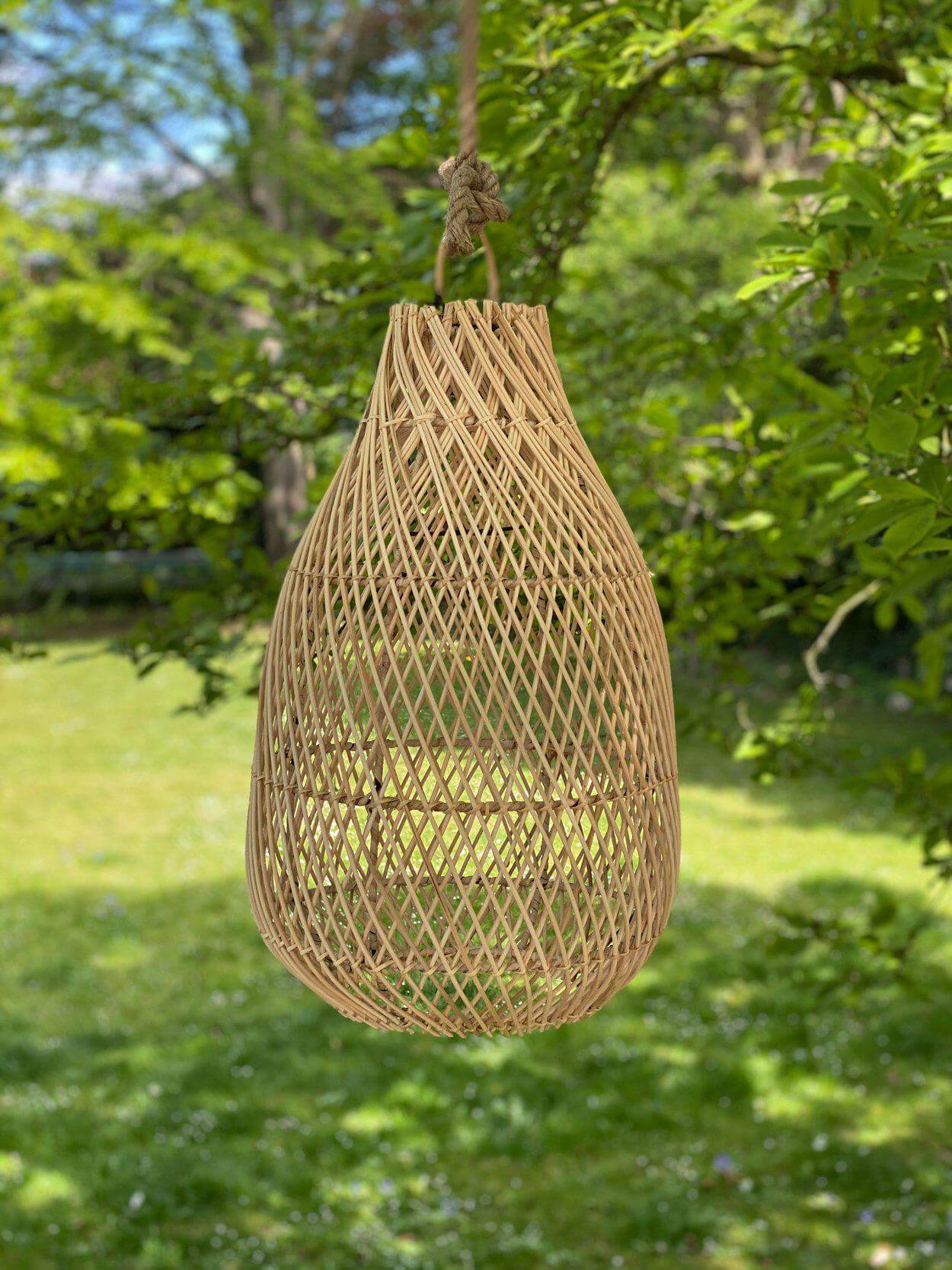 Rotan hanglamp Kendi in vaasvorm, handgemaakt en duurzaam, hangend in een groene buitenomgeving voor een bohemian sfeer.