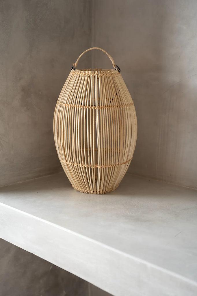 Rotan hanglamp The Zuri in klokvorm op grijze achtergrond, stijlvol en veelzijdig als hanglamp of vloerlamp. Perfect voor sfeervol wonen.