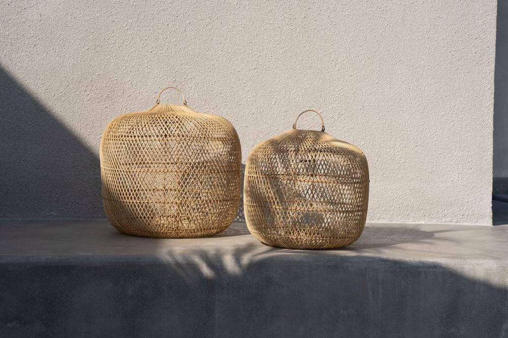 Twee rotan Batu Bolong lampenkappen op een grijze ondergrond in natuurlijk licht.