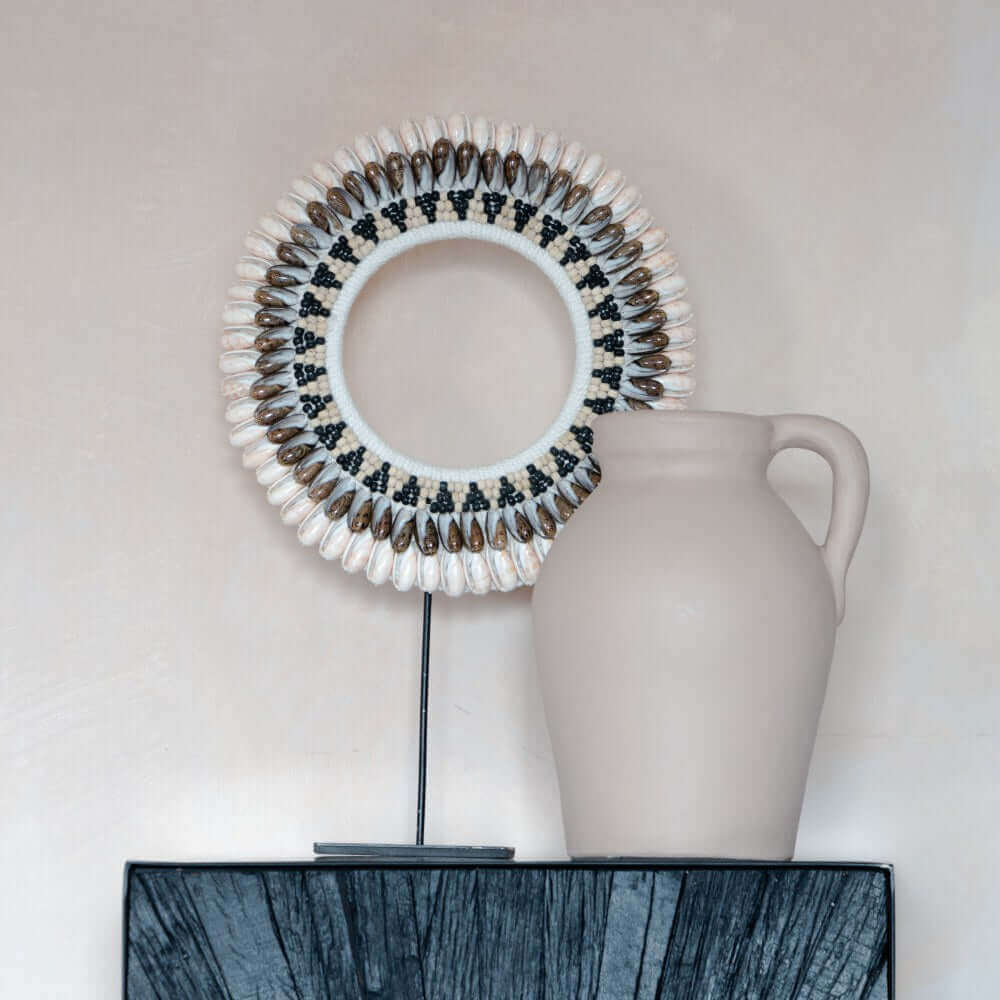Uniek ontworpen schelpenketting op standaard Citra met handgemaakte details, gecombineerd met keramische vaas, perfect voor interieurdecoratie.