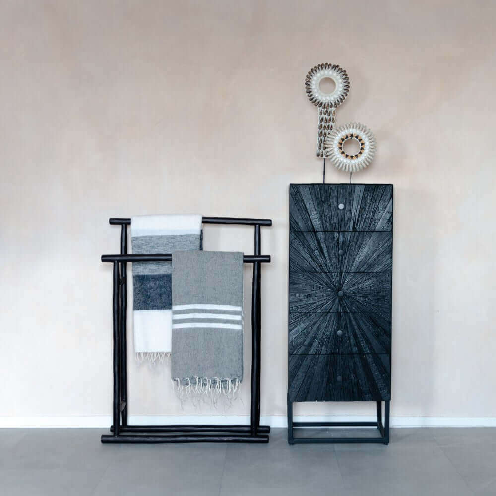 Schelpenketting op standaard Dasi in moderne interieurinstelling met zwarte kast en decoratieve handdoekenrek.