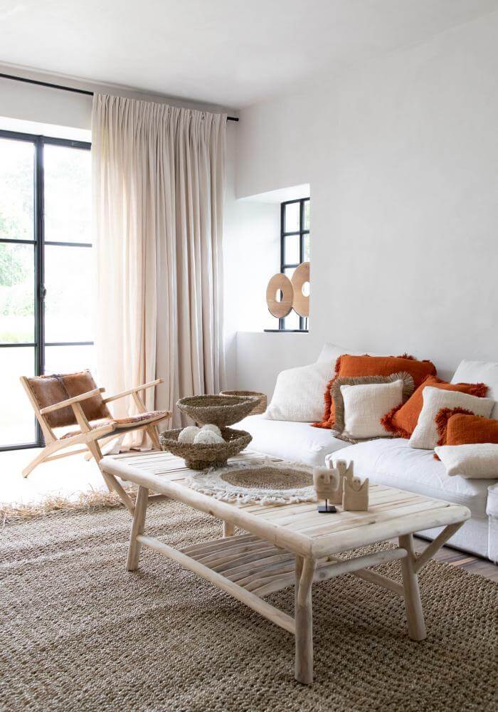 Stijlvol Ibiza interieur met natuurlijke toetsen, teakhouten decoratieve cirkel op standaard, en gezellige kussens op een lichte bank.