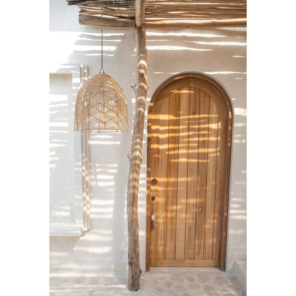 De Bala Hanglamp in rotan, boho stijl, hangt bij een houten deur, perfect voor binnen of overdekt terras. Exclusief bedrading.