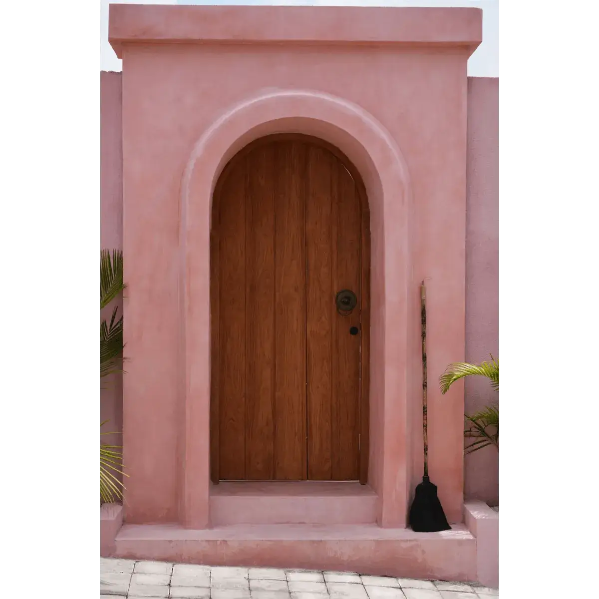 Bohemian style: The Big Broom in zwart, a decorative Indonesian grass broom by Bazar Bizar Living, displayed against a rustic pink archway.