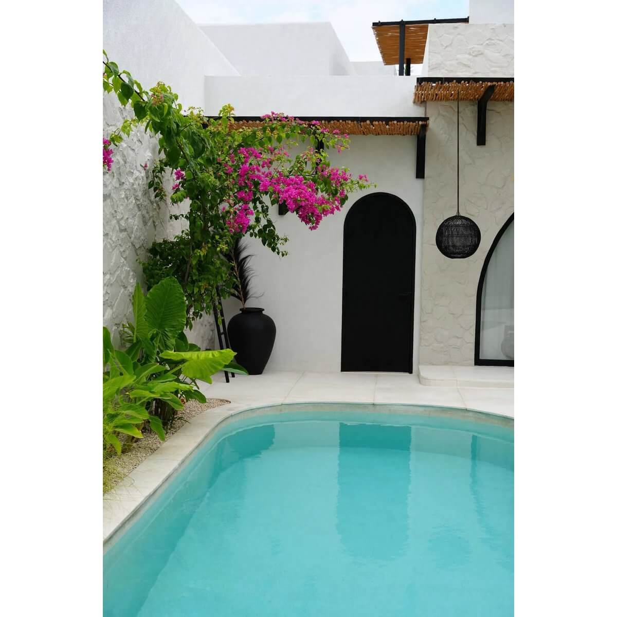 Zwembad met moderne tuinarrangementen en een zwarte rieten lamp, ideaal voor moderne, bohemien of eigentijdse interieurs.