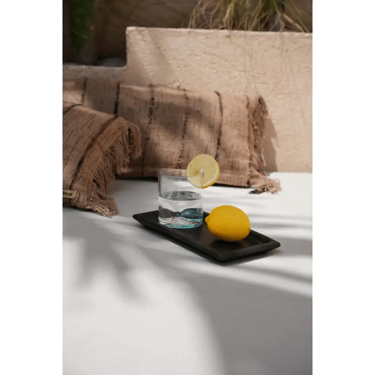 Bohemian style black terracotta sushi board with lemon and drink, stylish outdoor setting, by Bazar Bizar Living.