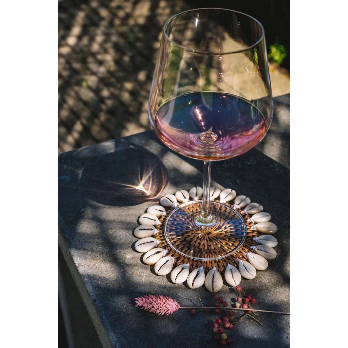 Bohemian rattan shell coaster with kauri shells under wine glass, adding tropical island touch to table setting.