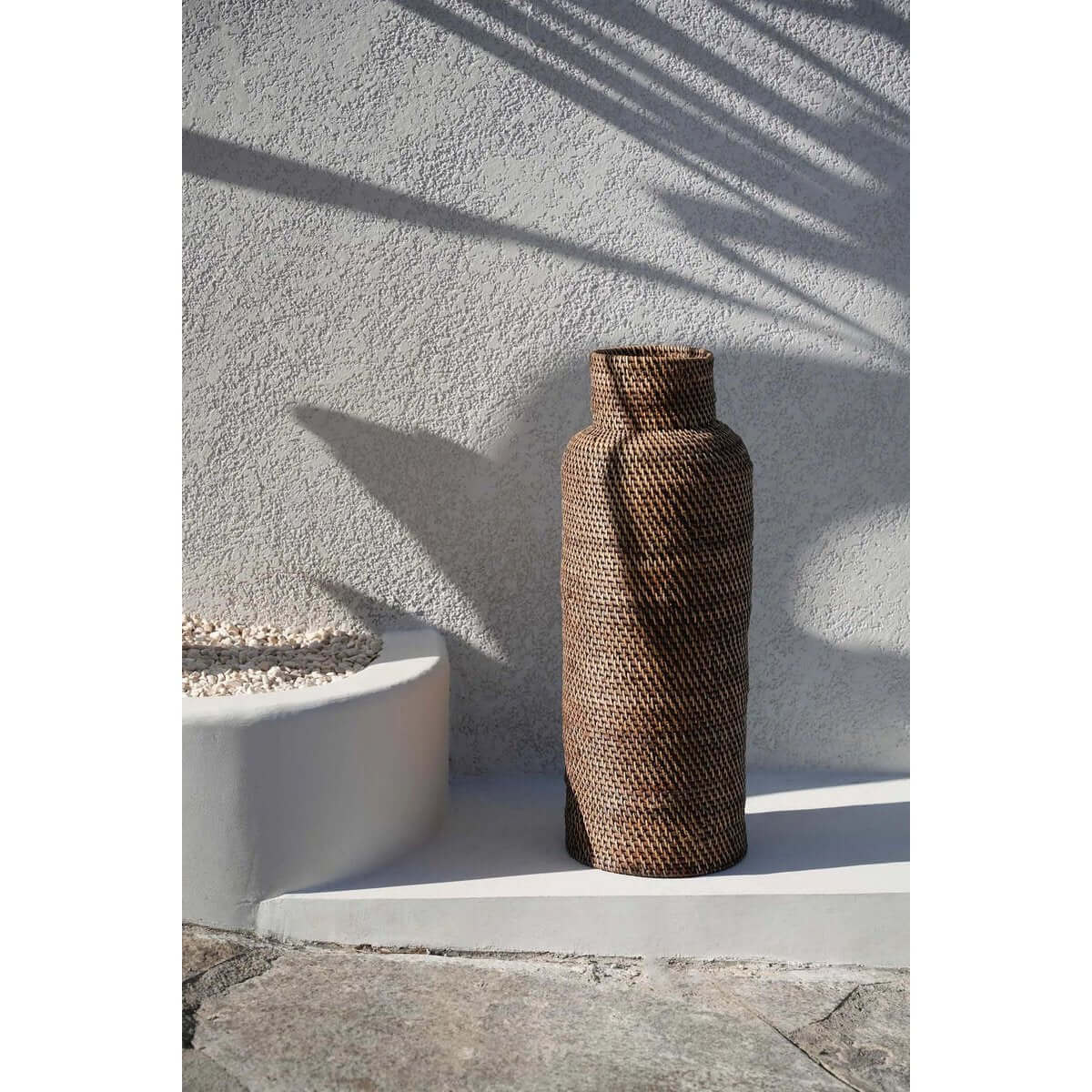 Koloniaal parasolmand van riet in natuurlijk bruin, staand op een betonnen ondergrond in zonlicht.