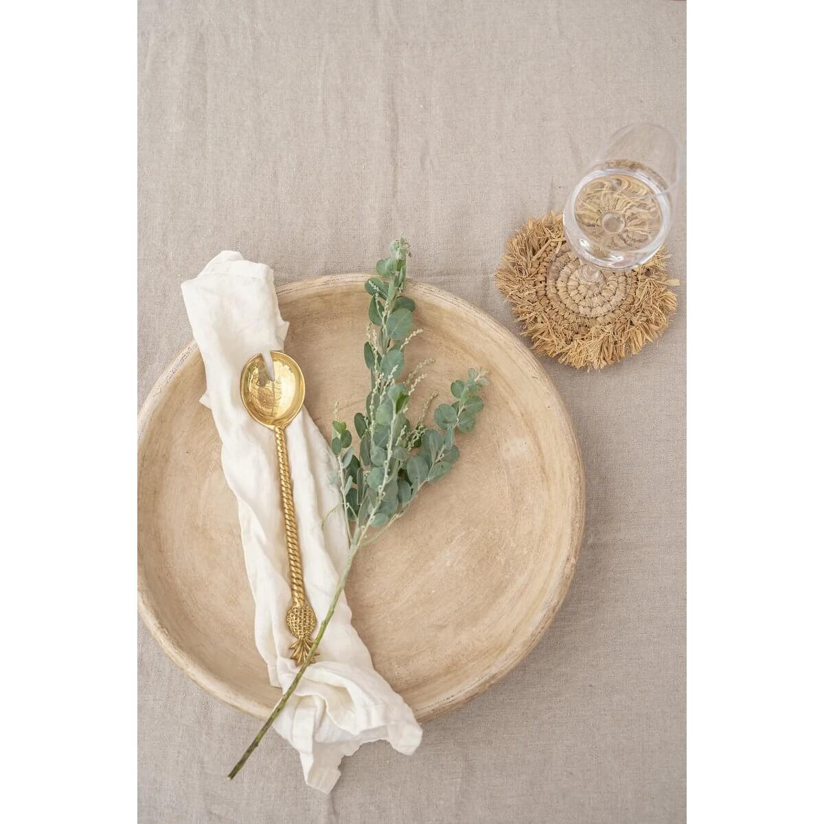 Bohemian Fringe Raffia Coaster on table with rustic decor, perfect for interior styles; includes gold spoon, white cloth, and eucalyptus.