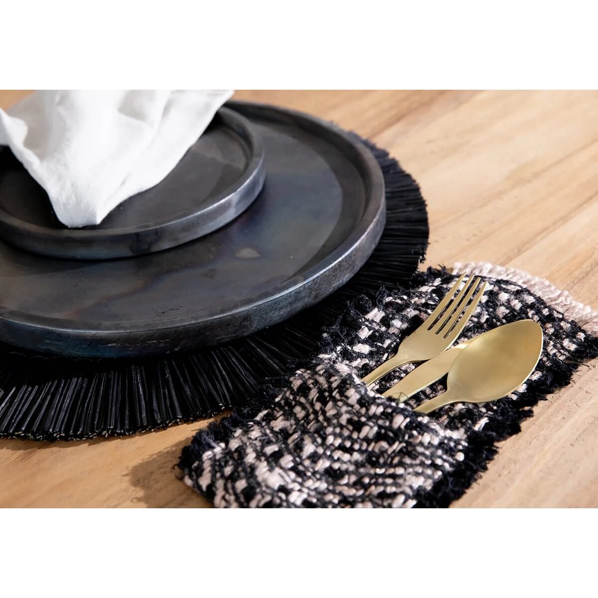 Luxe Bohemian bestekhouder set van vier op tafel met zwart koper en katoenen zijdelook, naast een zwarte ronde onderzetter.