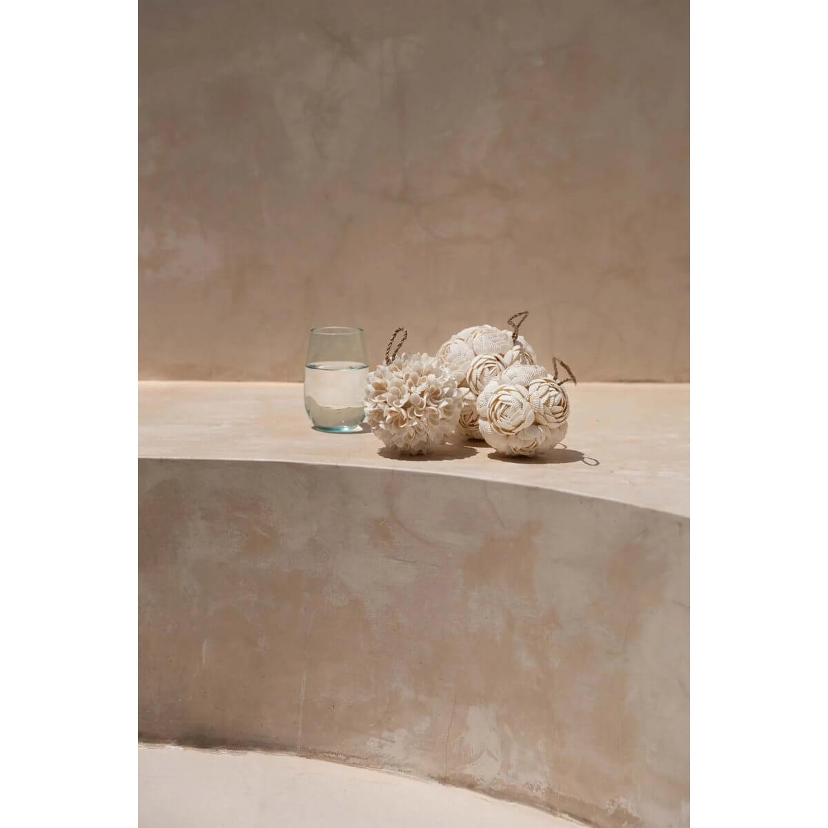 Bohemian decor with handcrafted white rose shell balls and glass of water on a minimalist surface.