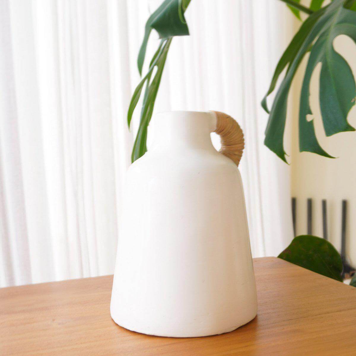 Stijlvolle witte vaas met een natuurlijke uitstraling, perfect voor boho-interieurs, op een houten tafel voor een lichte gordijnachtergrond.