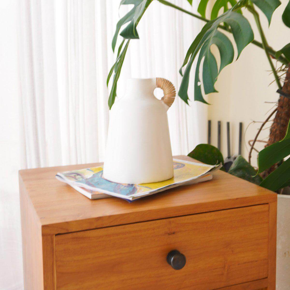 Witte vaas op houten kastje naast groene plant voor een frisse, moderne inrichting.