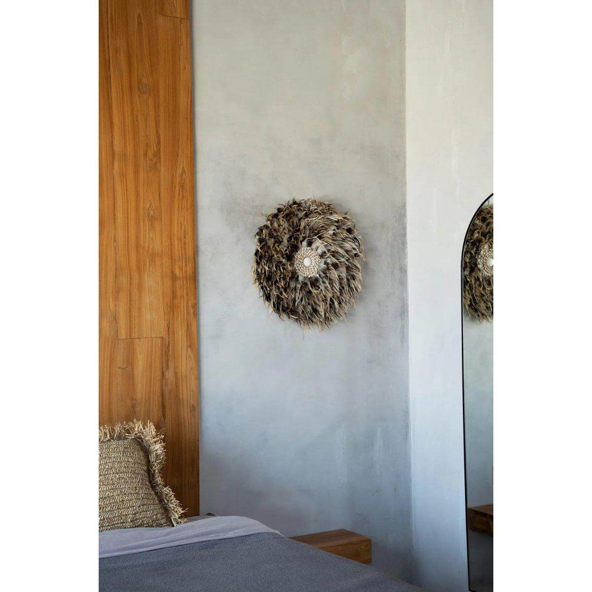 Bohemien wanddisplay met grijsbruine veren en schelpen, hangt op een muur naast een gezellige slaapkamer setting.
