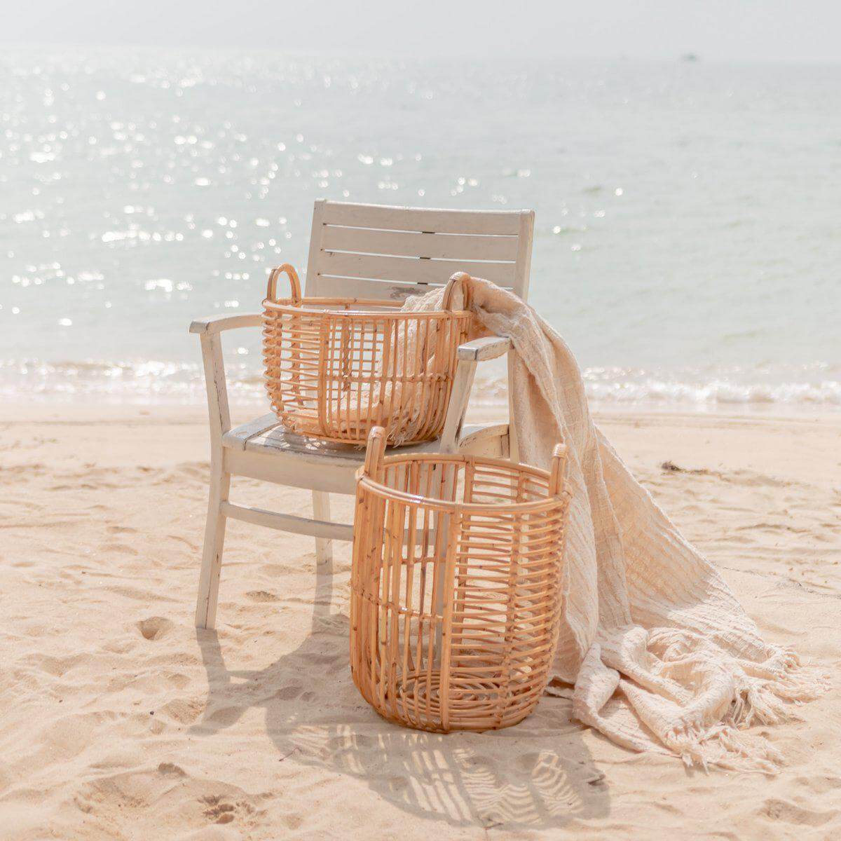 Opbergmand JEMUH van rotan op strand met stoel en deken, perfect als wasmand, duurzaam en handgemaakt, twee maten beschikbaar.