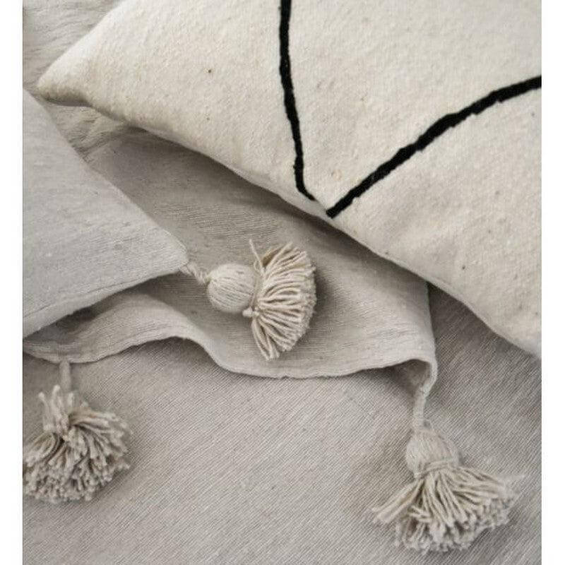 Marokkaanse pom pom deken en kussen in crème tinten voor een gezellig interieur.